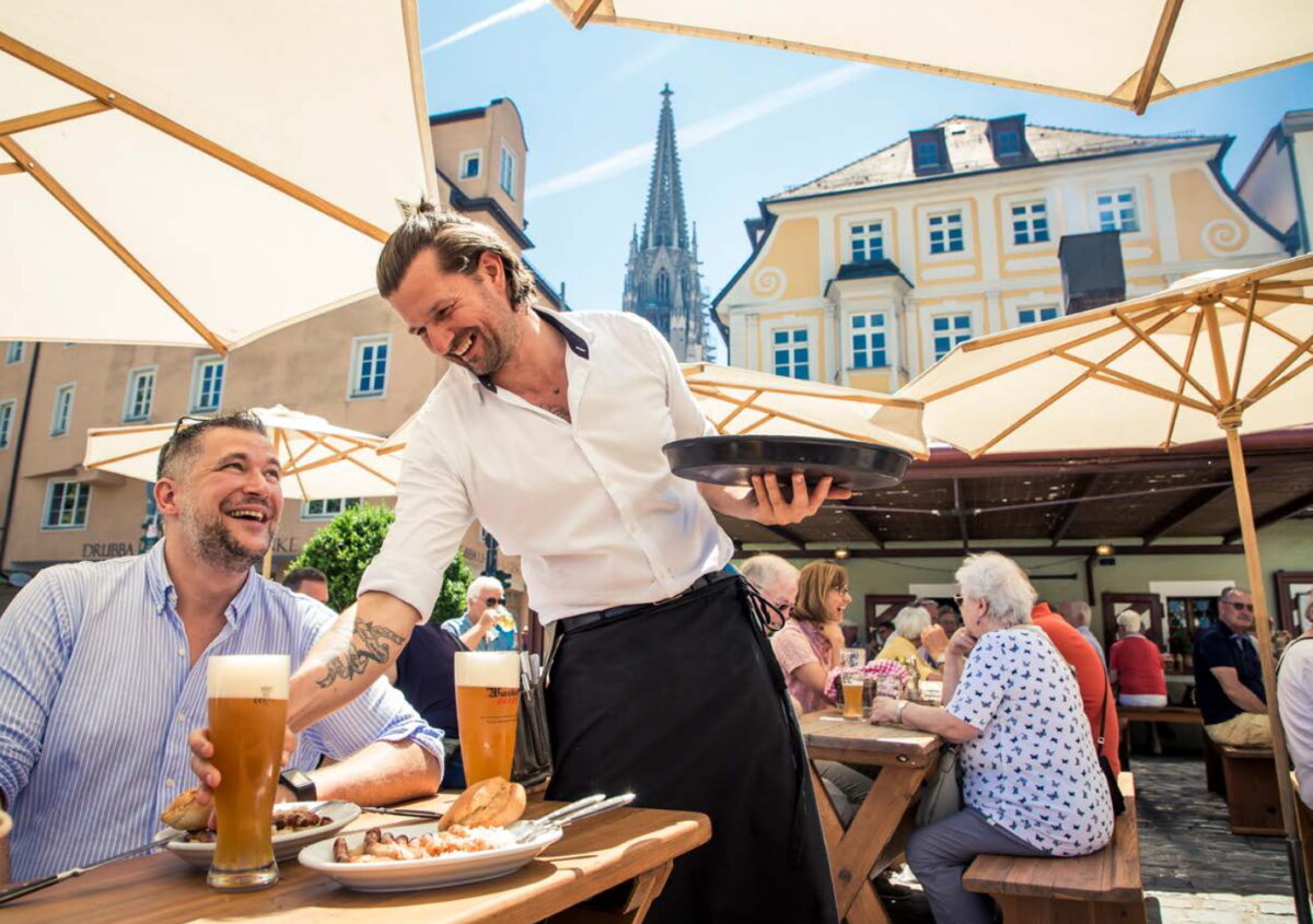 Szene im Freien: Kellner stellt einem Mann ein Weißbier auf den Tisch