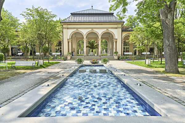 Blick auf einen langen Pool mit blauen Fliesen und eine Pagode im Hintergrund. 