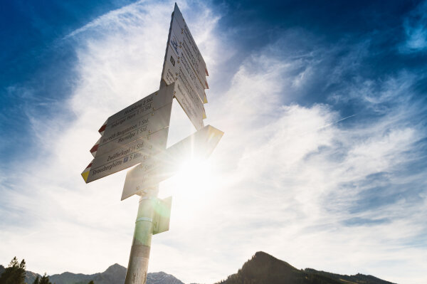 Wegweiser mit vielen Schildern und der Sonne im Hintergrund.