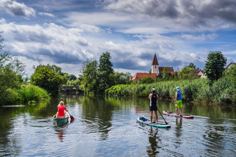 Eine Person in einem Kajak und zwei Personen auf Paddle-Boards auf einem Fluss.