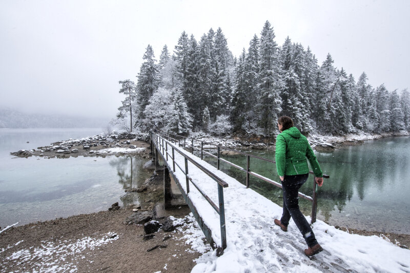 Eine Person läuft über eine verschneite Brücke an einem See.