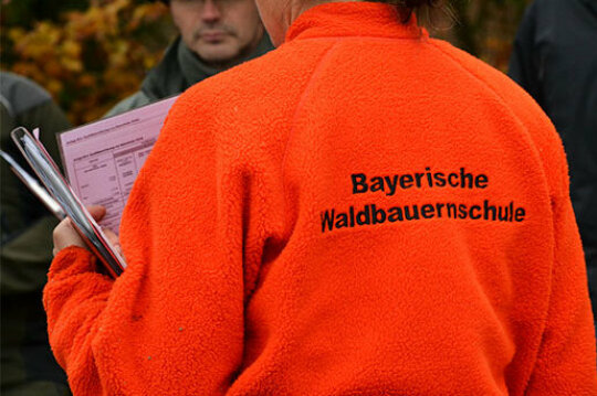 Person mit oranger Jacke und Aufschrift "Bayerische Waldbauernschule"