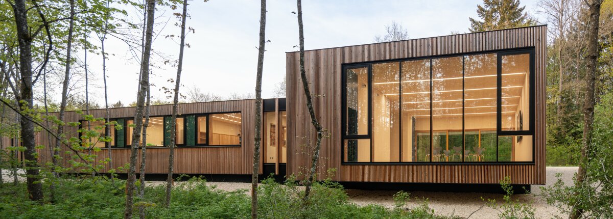Holzbau mit großen Fensterfronten umgeben von Wald