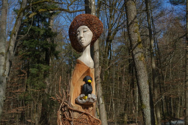 Holzskulptur einer Person mit einem Raben im Wald