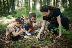 Försterin zeigt Kindern etwas am Waldboden