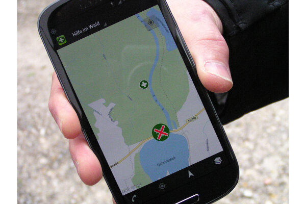 Nahaufnahme einer Hand mit Smartphone, auf dem die App "Hilfe im Wald" geöffnet ist 