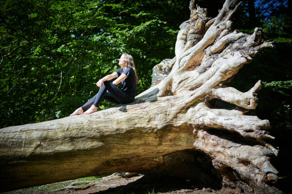 Eine Frau sitzt auf einem großen entwurzelten Baum in der Sonne